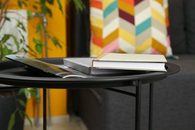 Books and notebook on black table near sofa indoors, closeup