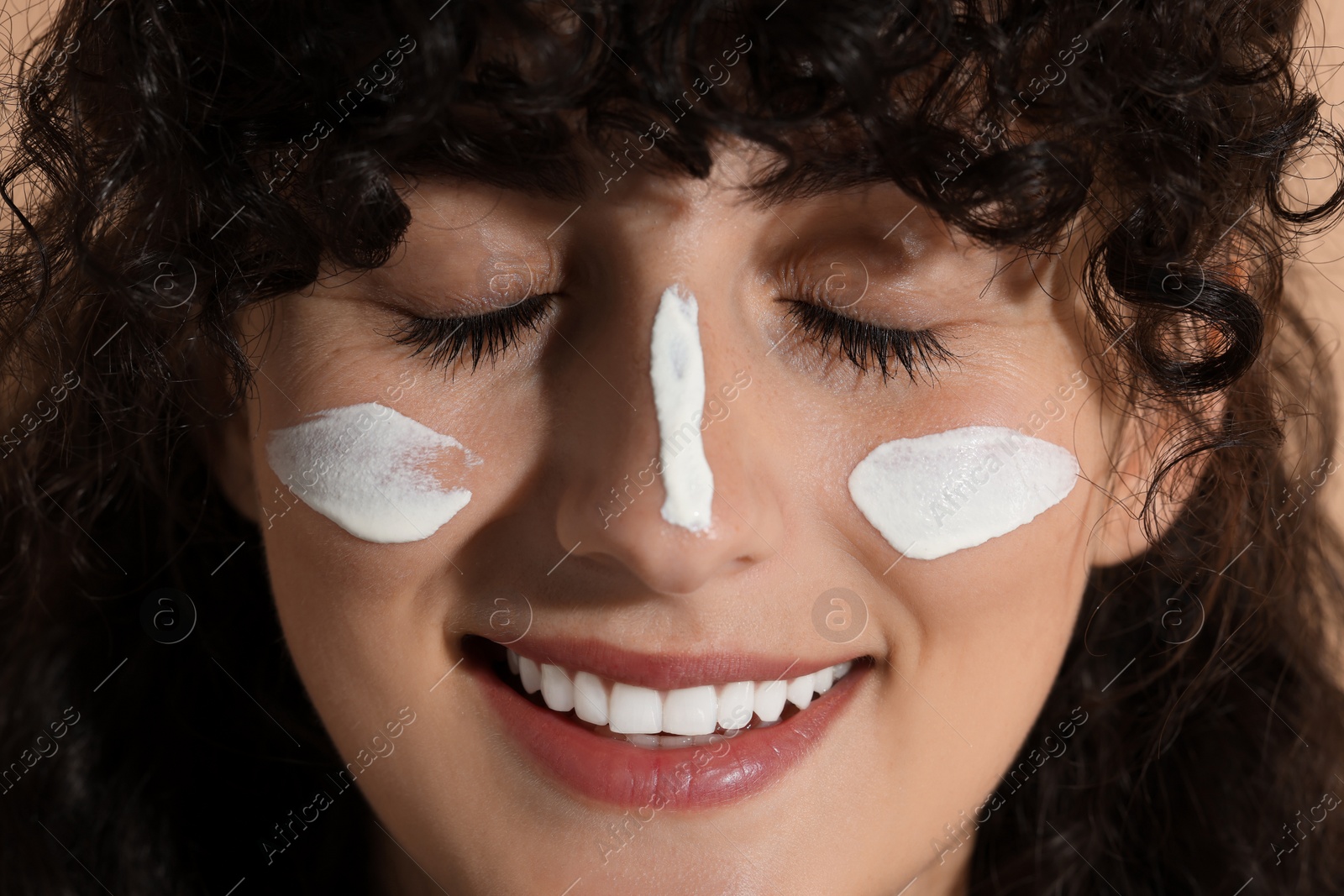 Photo of Beautiful young woman with sun protection cream on her face against beige background, closeup