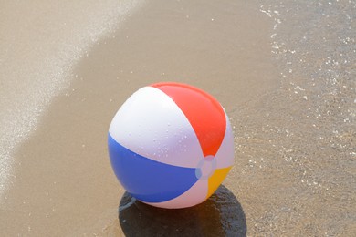 Photo of Colorful beach ball on wet sand at seaside