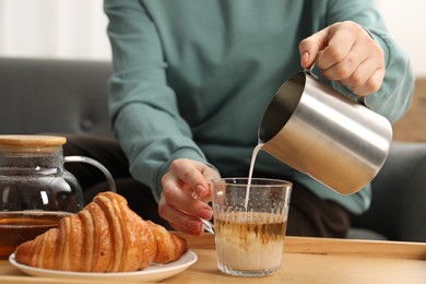 Photo of Woman pouring milk into cup with aromatic tea at table indoors, closeup