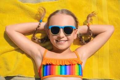 Happy little girl in sunglasses enjoying sunny day on sandy beach, top view