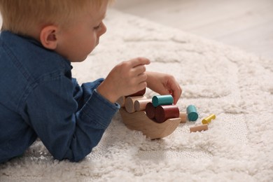 Photo of Little boy playing with wooden balance toy on carpet indoors, closeup