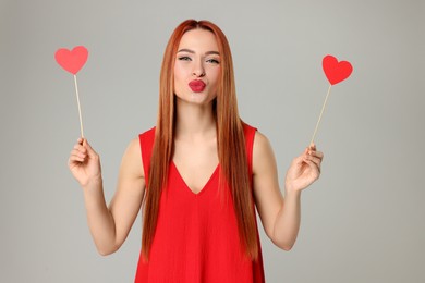 Photo of Young woman in red dress with paper hearts on light grey background