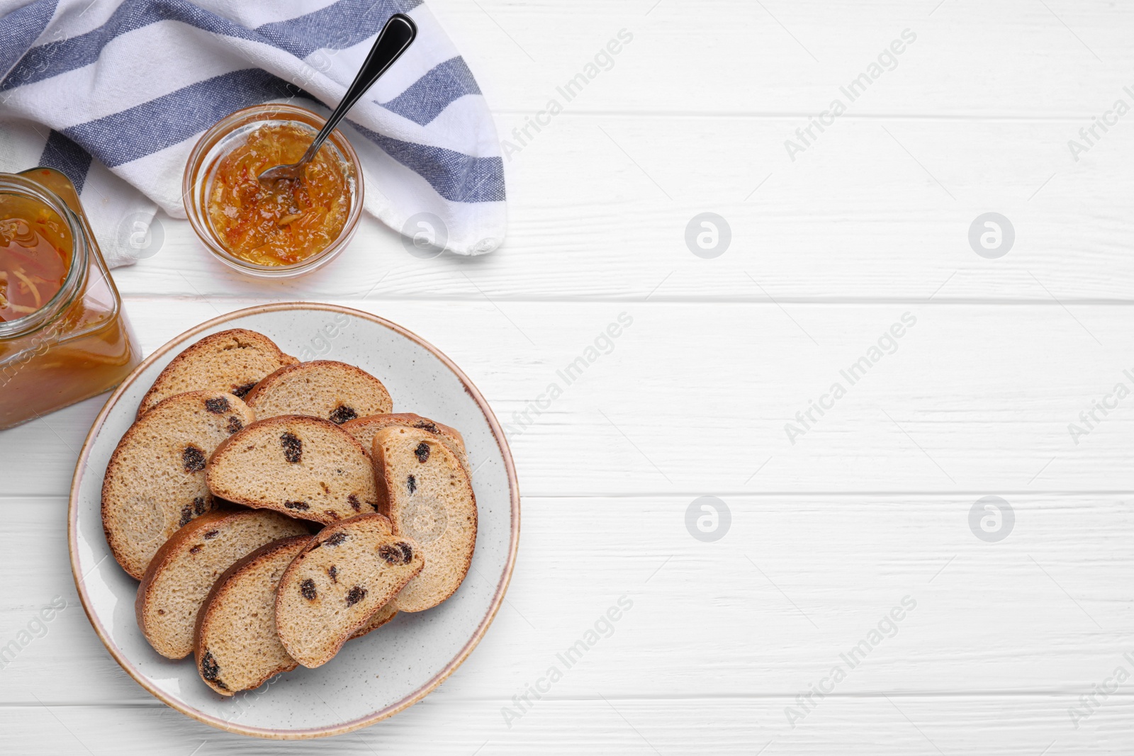 Photo of Plate of sweet hard chuck crackers with raisins and jam on white wooden table, flat lay. Space for text