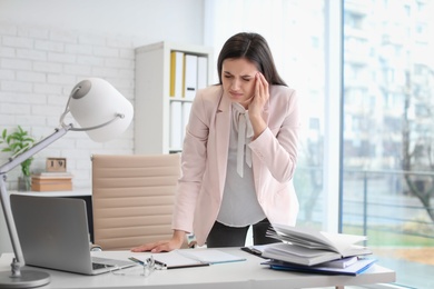 Photo of Young woman suffering from headache in office