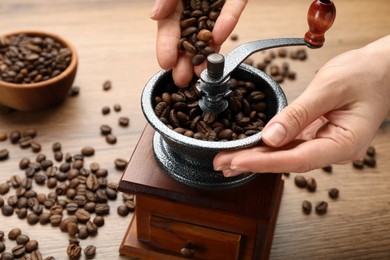 Photo of Woman using manual coffee grinder at wooden table, closeup