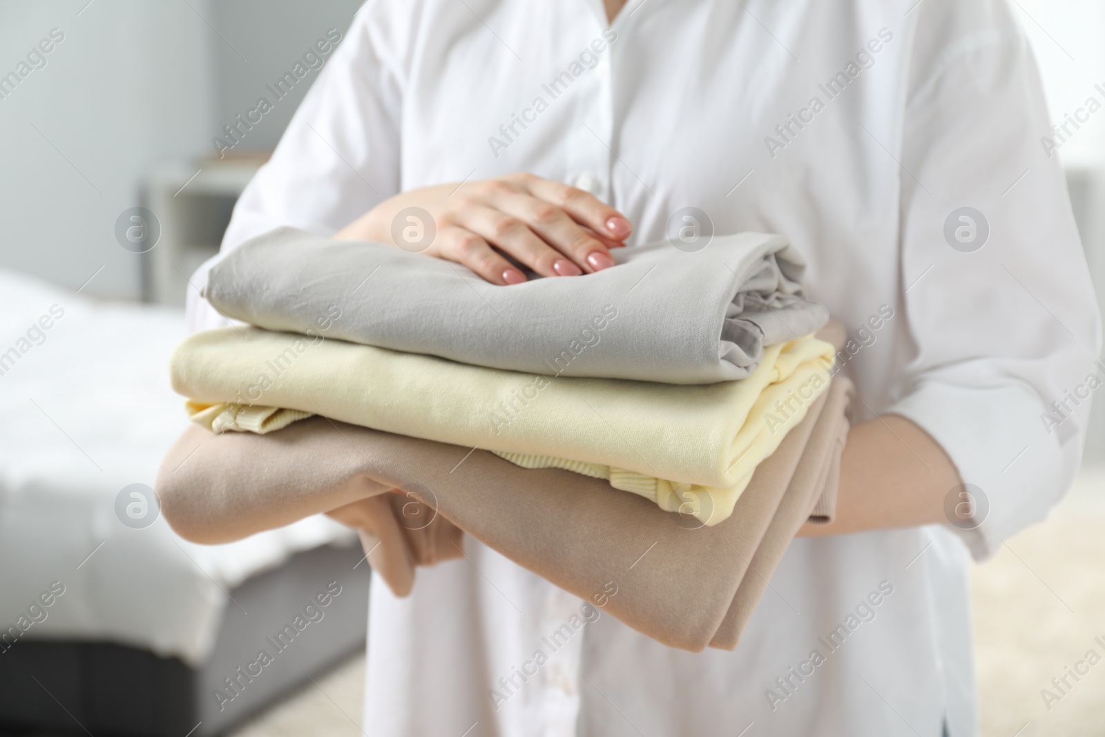 Photo of Woman holding folded clothes at home, closeup