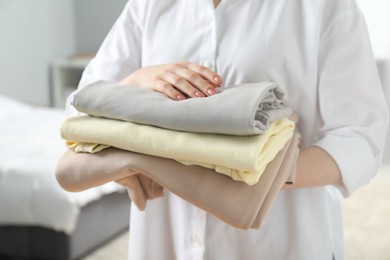 Woman holding folded clothes at home, closeup