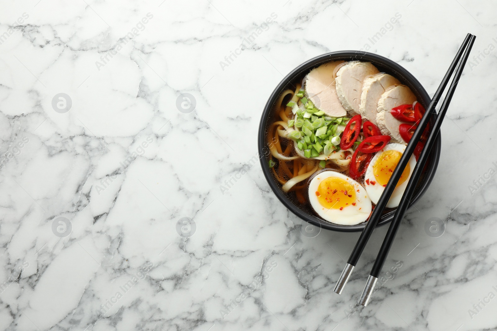 Photo of Delicious ramen in bowl on white marble table, top view with space for text. Noodle soup