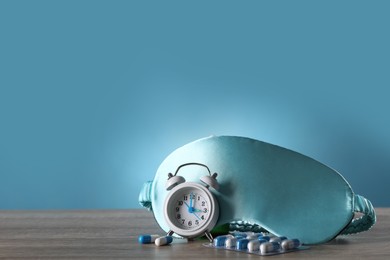 Photo of Sleeping mask, alarm clock and pills on wooden table. Insomnia treatment