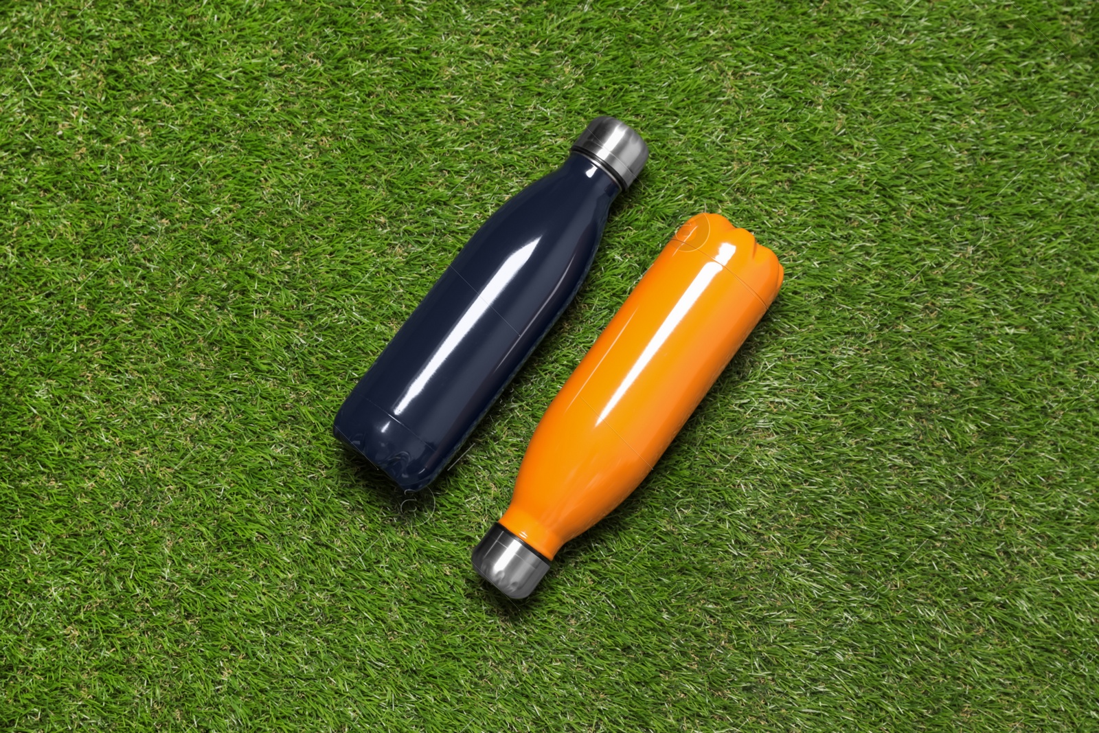 Photo of Modern thermos bottles on green grass, flat lay