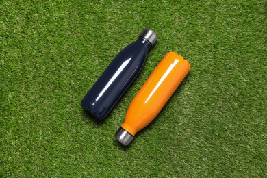 Modern thermos bottles on green grass, flat lay