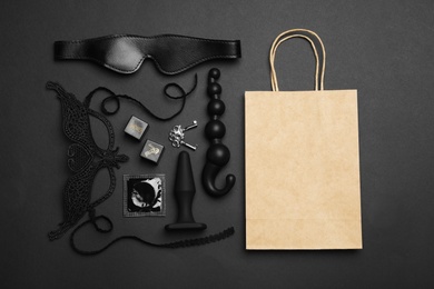 Photo of Shopping bag and different sex toys on black background, flat lay