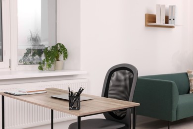 Photo of Stylish workplace with wooden table, chair and sofa in room. Interior design