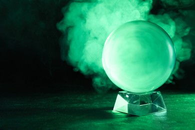 Photo of Crystal ball on table and smoke against dark background, space for text. Predictions of future