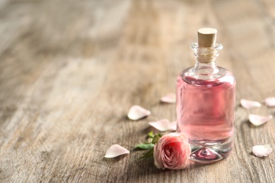 Photo of Bottle of rose essential oil and flower on wooden table, space for text