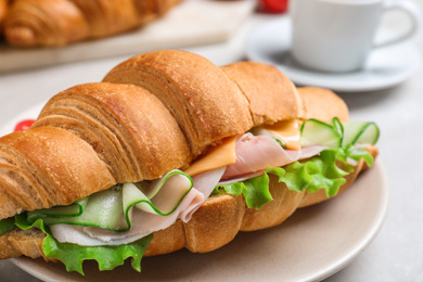 Tasty croissant sandwich with ham and cucumber on light table, closeup