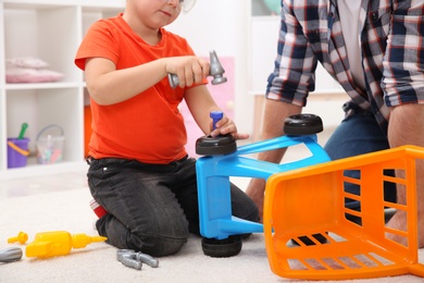 Man and his child as repairman playing with toy cart at home, closeup