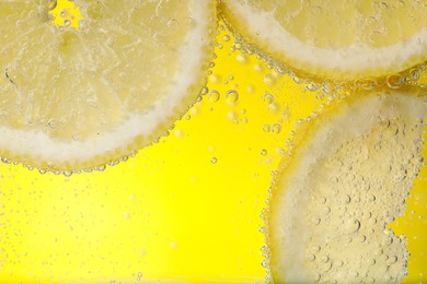 Photo of Juicy lemon slices in soda water against yellow background, closeup