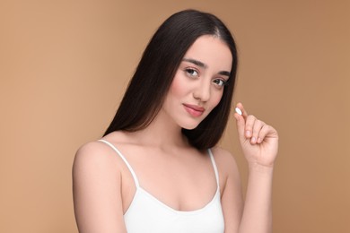 Photo of Beautiful young woman with vitamin pill on beige background