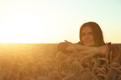 Photo of Beautiful young woman sitting in ripe wheat field on sunny day, space for text