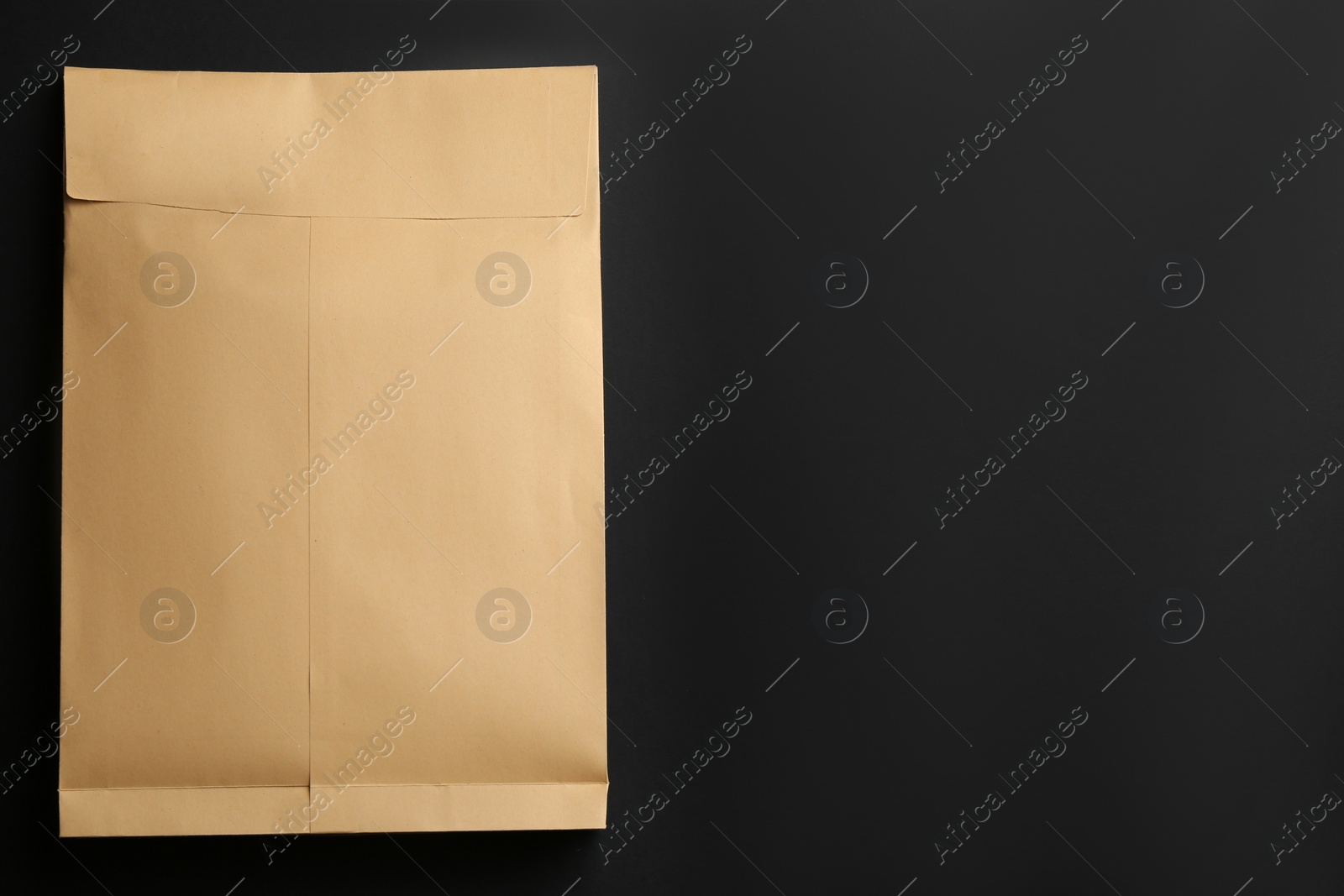 Photo of Kraft paper envelope on black background, top view. Space for text