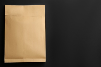 Photo of Kraft paper envelope on black background, top view. Space for text
