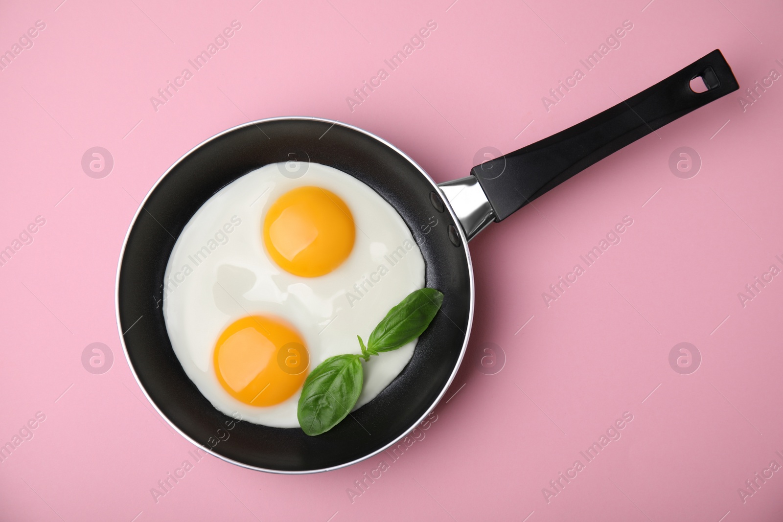 Photo of Tasty fried eggs with basil in pan on pink background, top view