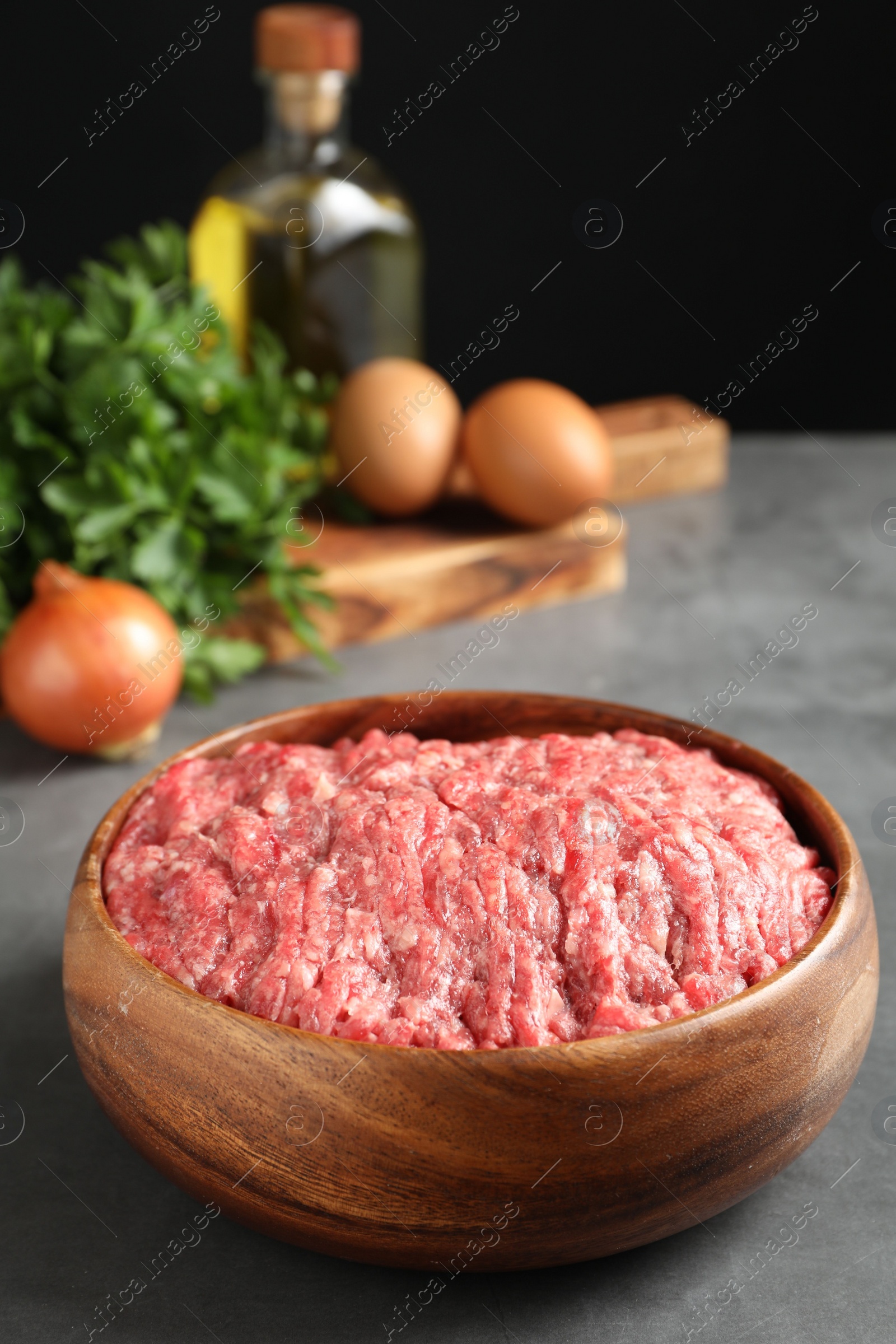 Photo of Raw ground meat in bowl and different products on grey table