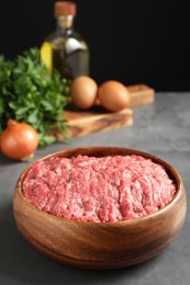 Raw ground meat in bowl and different products on grey table