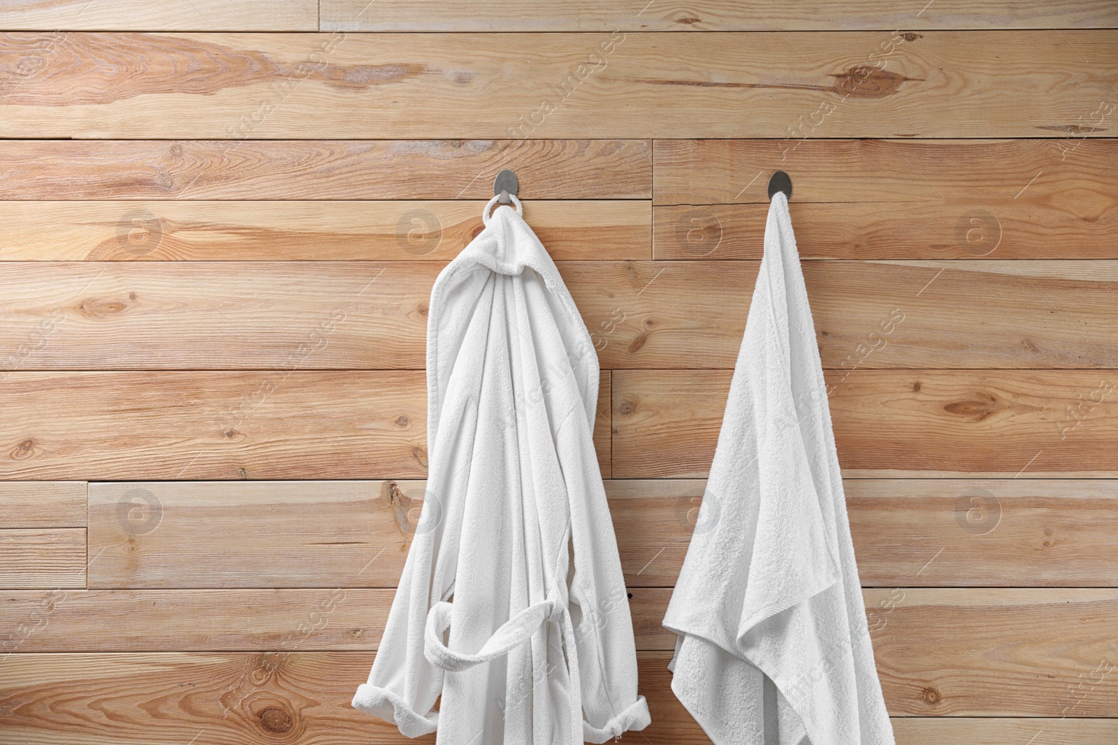 Photo of Soft comfortable bathrobe and towel hanging on wooden wall
