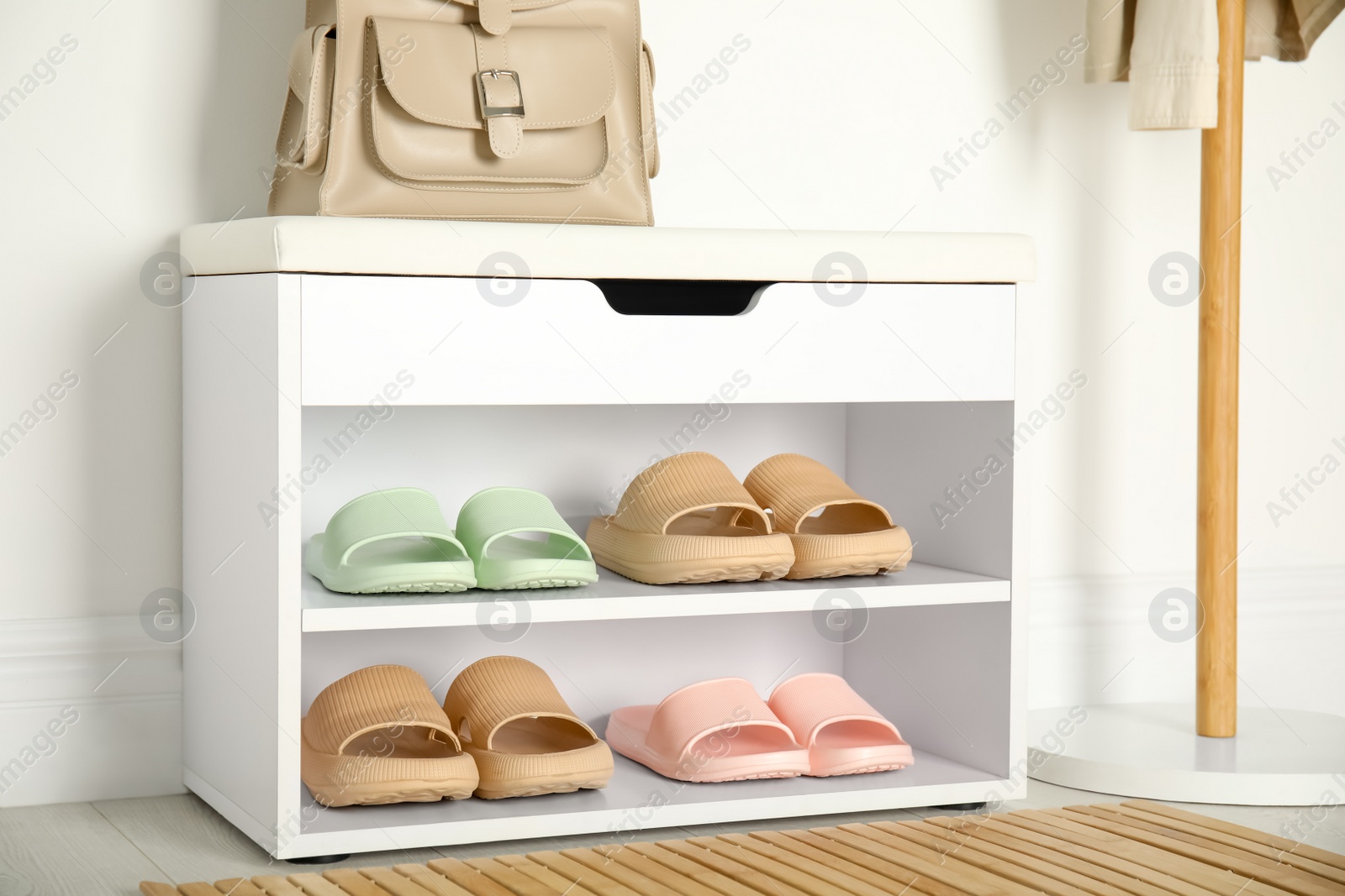 Photo of Storage cabinet with different pairs of rubber slippers near white wall in room