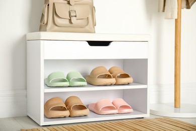 Storage cabinet with different pairs of rubber slippers near white wall in room