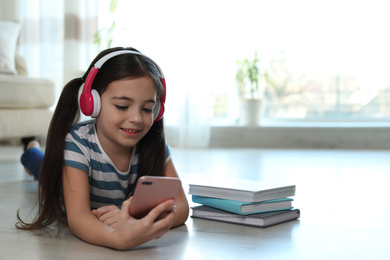 Cute little girl with headphones and smartphone listening to audiobook at home