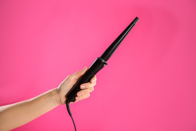 Photo of Woman holding clipless curling hair iron on pink background, closeup