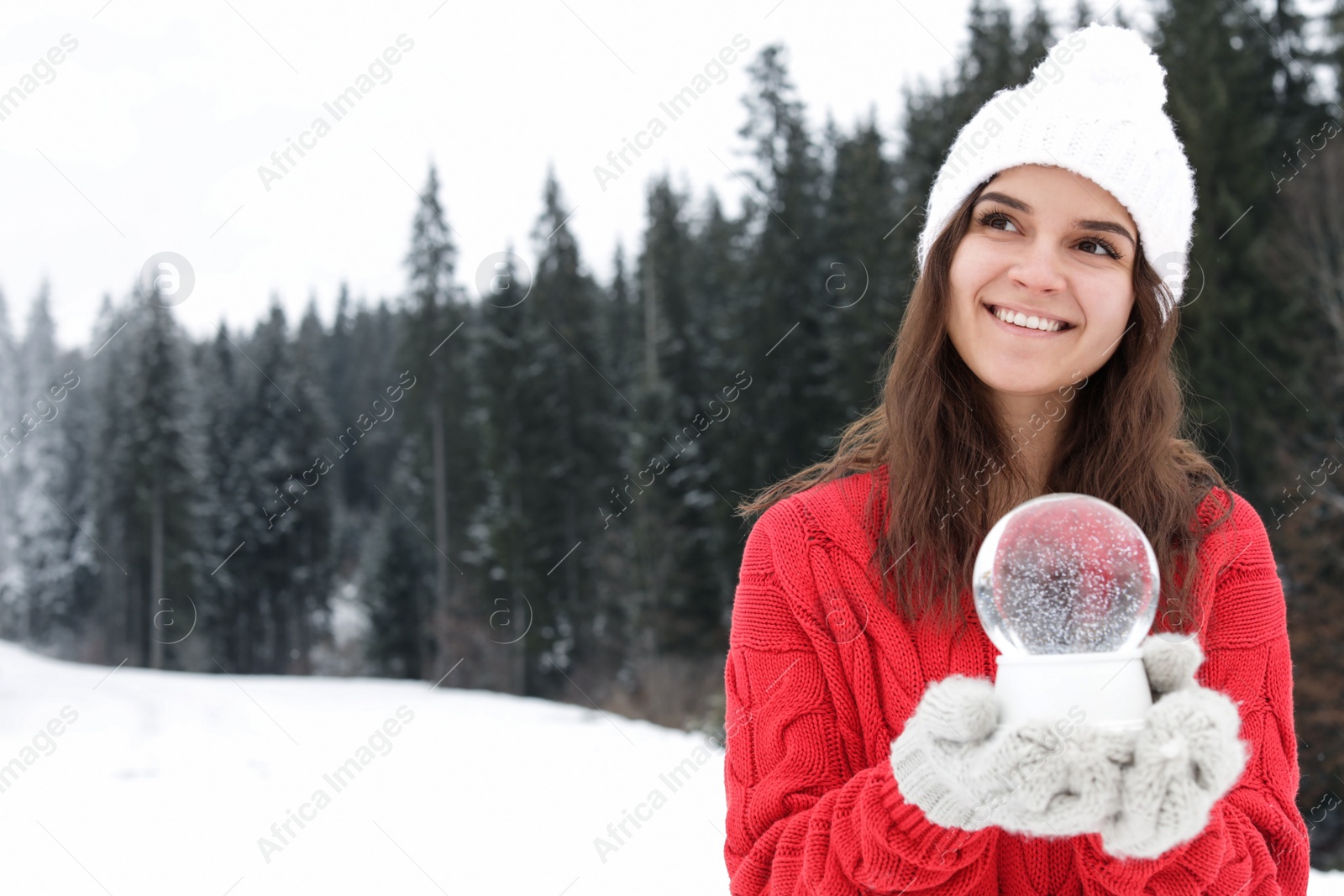 Photo of Young woman in knitted clothes holding snow globe outdoors, space for text. Winter vacation