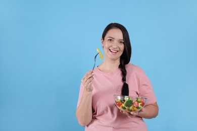Photo of Beautiful overweight woman eating salad on light blue background, space for text. Healthy diet