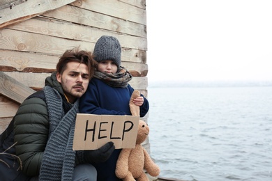 Photo of Poor father and child with HELP sign at riverside. Space for text