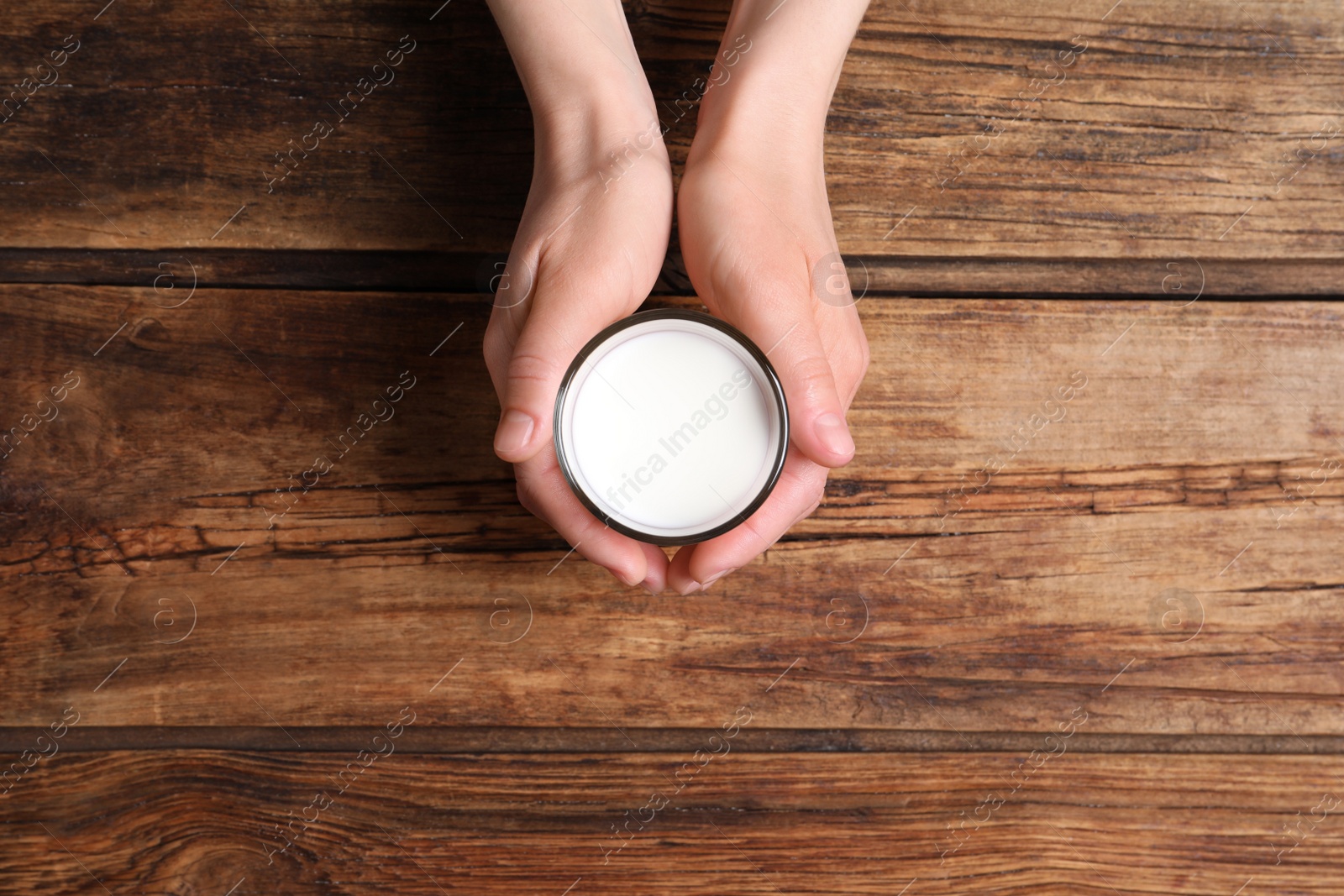 Photo of Woman holding glass of milk at wooden table, top view