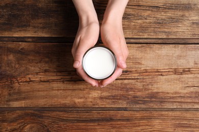 Photo of Woman holding glass of milk at wooden table, top view