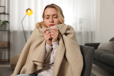 Photo of Sick woman wrapped in blanket with tissue in armchair at home. Cold symptoms