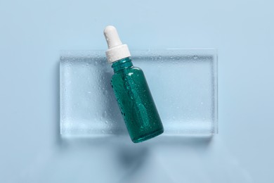 Photo of Bottle of cosmetic serum on light blue background, top view