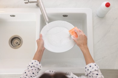 Photo of Woman washing plate above sink in modern kitchen, top view