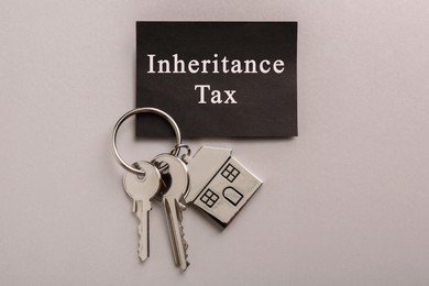 Photo of Card with phrase Inheritance Tax and keys with house shaped key chain on grey background, top view