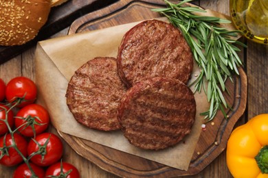 Photo of Tasty grilled hamburger patties, vegetables and rosemary on wooden table, flat lay