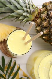 Tasty pineapple smoothie and fruit on white wooden table, flat lay