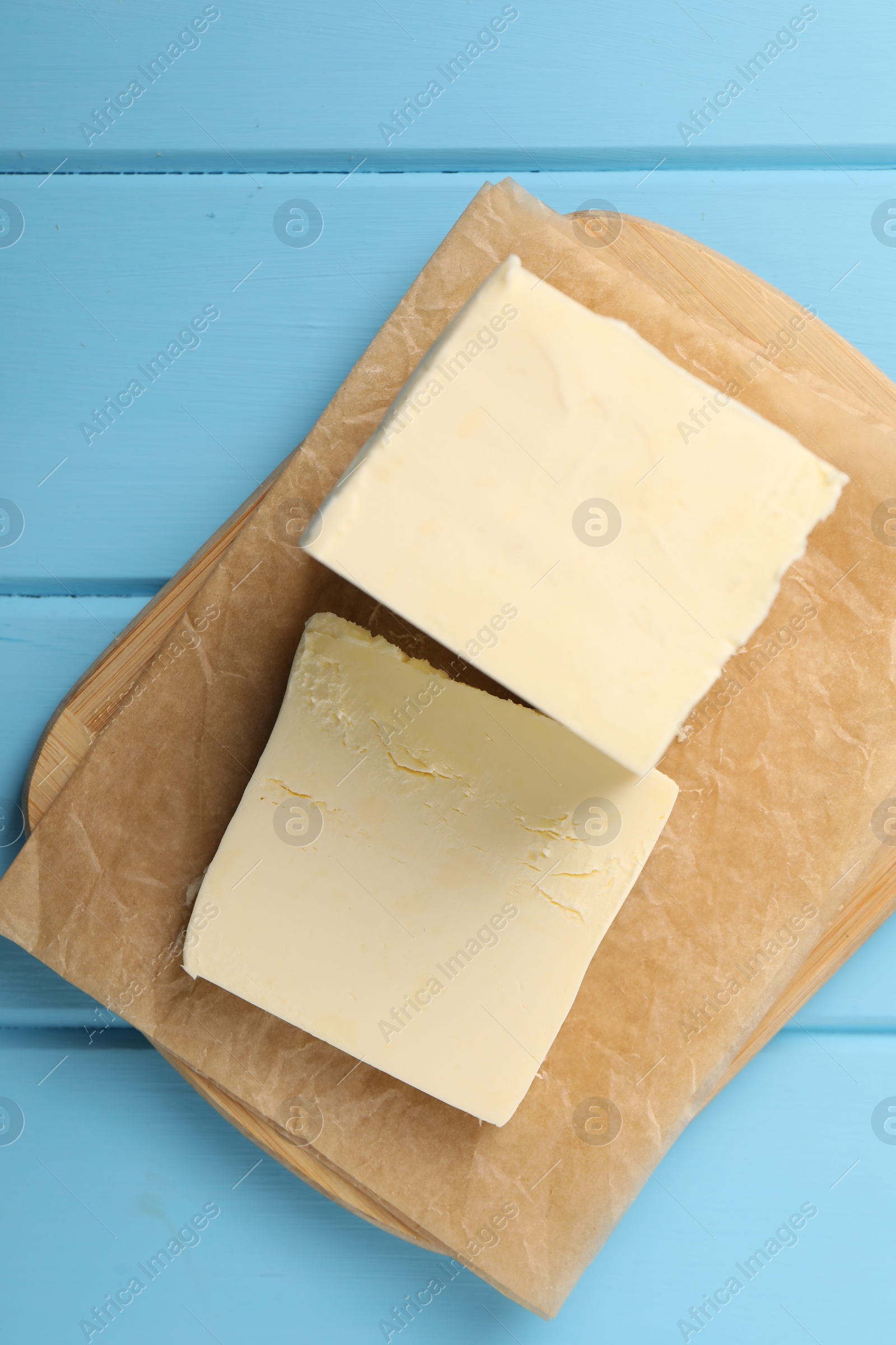 Photo of Block of tasty butter on light blue wooden table, top view