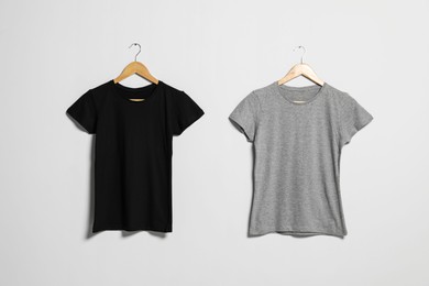 Photo of Hangers with different t-shirts on light wall. Mockup for design
