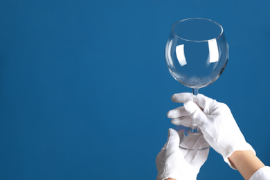 Photo of Person in white gloves checking cleanliness of glass on blue background, closeup. Space for text