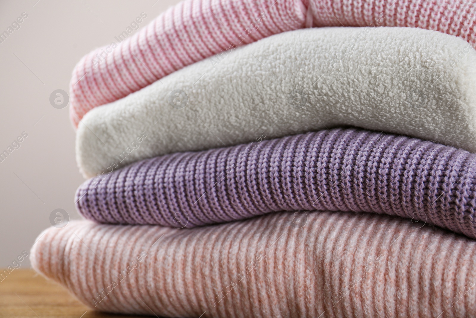 Photo of Stack of knitted sweaters on wooden table, closeup